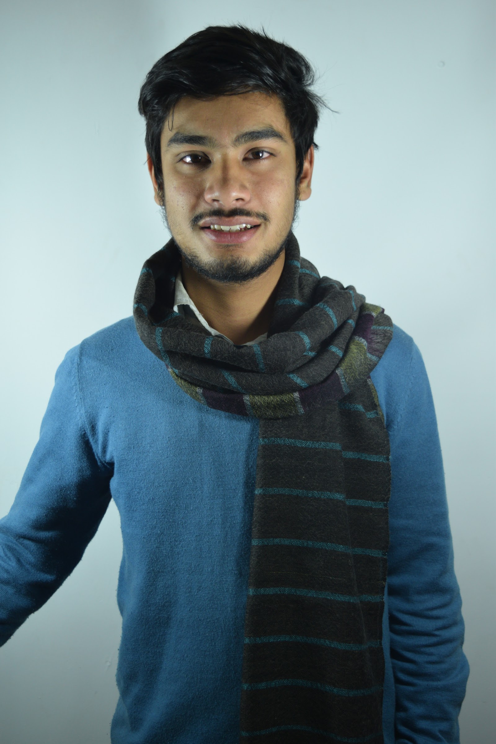 Man wearing a dark striped woven cashmere scarf over a blue sweater